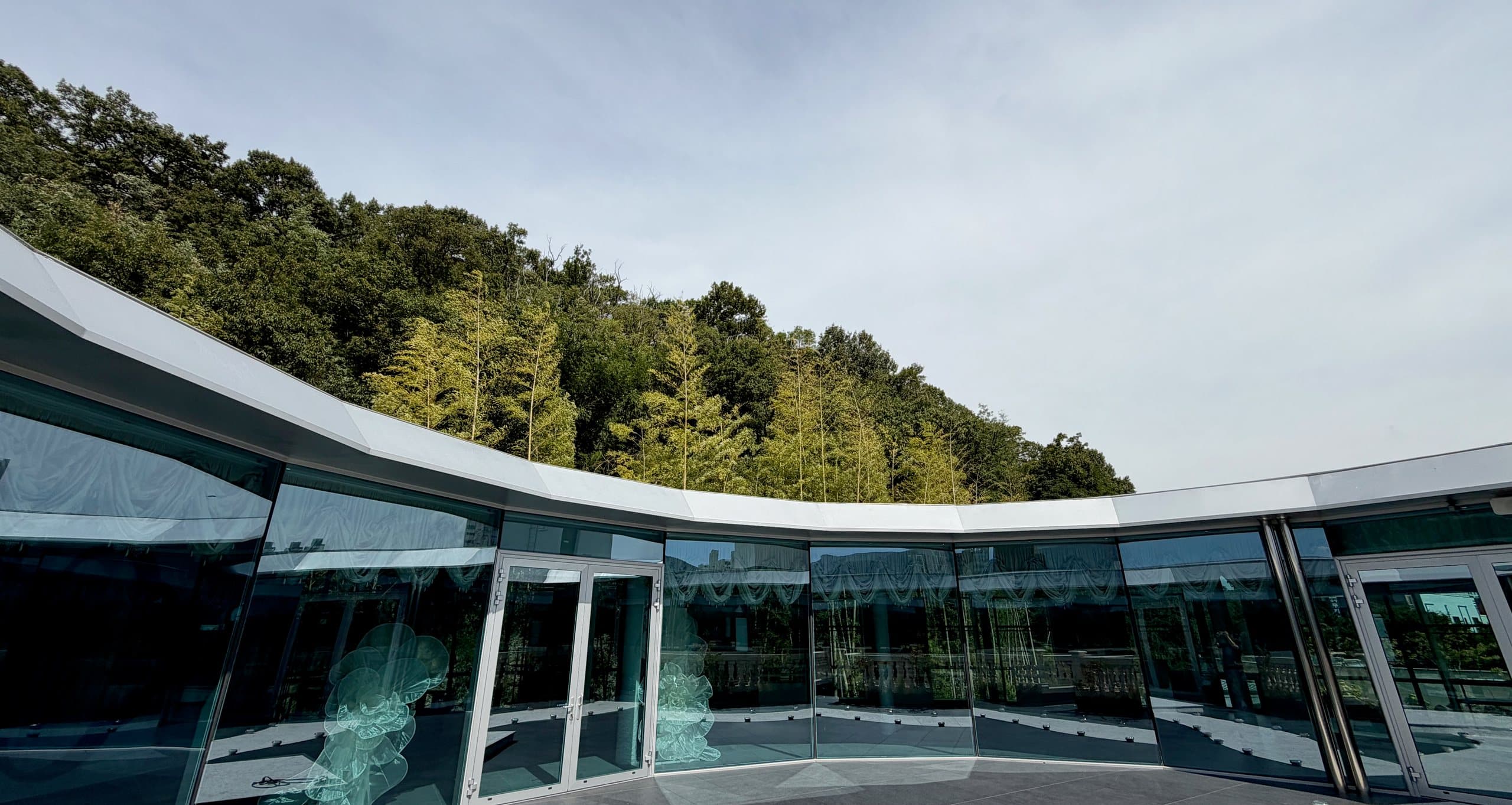 The circular glass pavilion against the wooded hillside